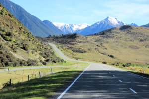 Open road stretching toward snow-capped mountains, flanked by rolling green hills—capturing the spirit of adventure ideal for blog posts about the best travel apps or best apps for planning a road trip.