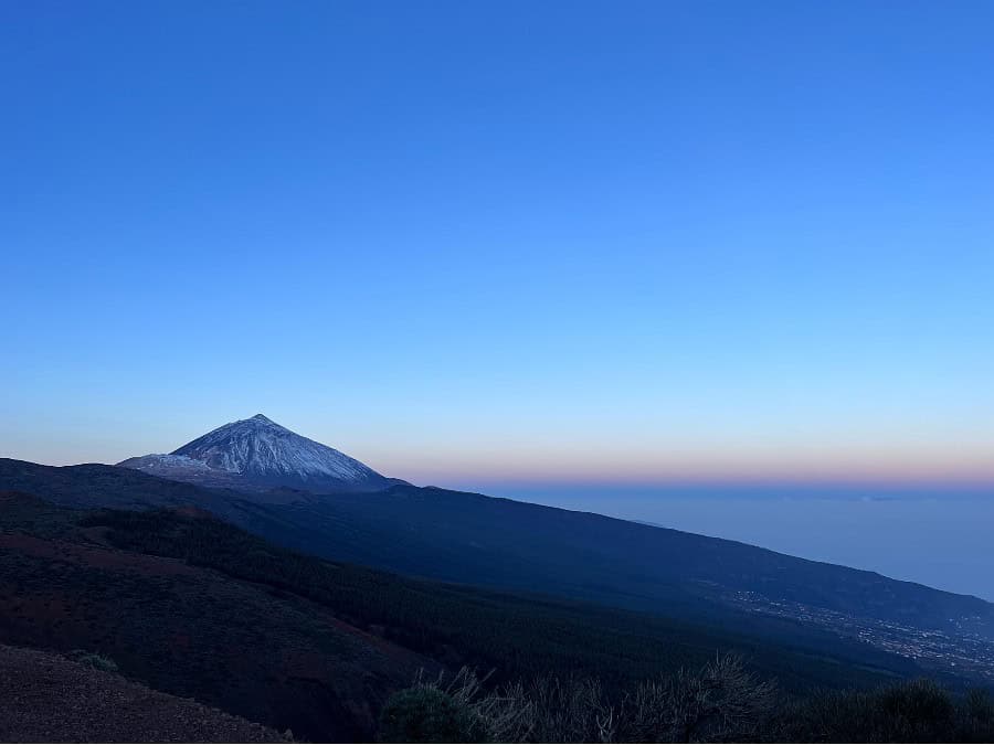 Mount Teide at dawn in Tenerife, with soft pastel sky and dark hillside in the foreground.