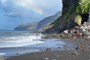 a black sand beach with a rainbow in the sky