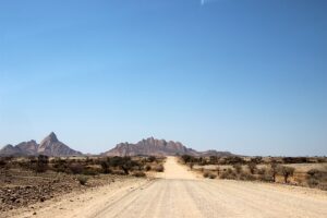 long empty gravel road with the granite peaks of Spitzkoppe in the distance
