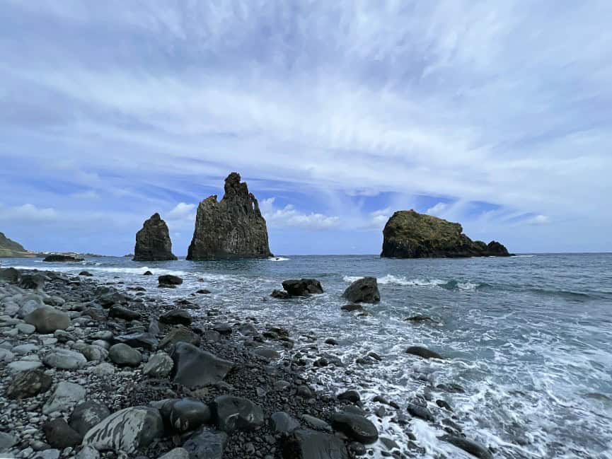 Dramatic view of sea stacks at Ribeira da Janela beach on Madeira’s north coast, with large black pebbles in the foreground and waves crashing on the rugged shoreline.