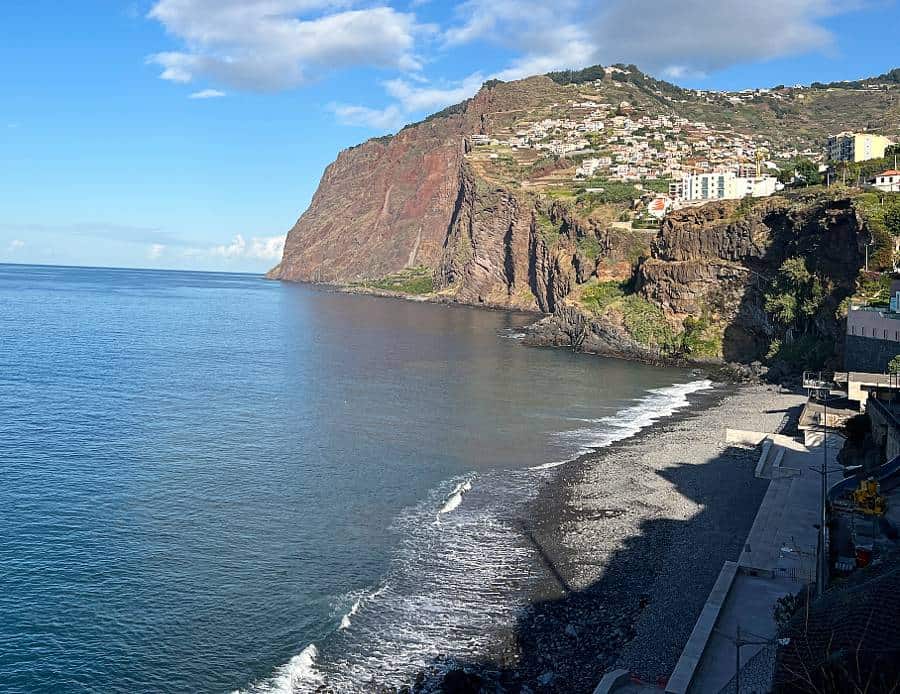 Pebble beach at Vigário in Câmara de Lobos, backed by cliffs with colourful homes on the hillside.