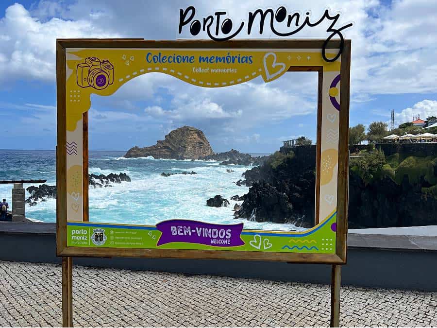 View of the Atlantic Ocean and volcanic coastline framed by the Porto Moniz welcome sign, Madeira