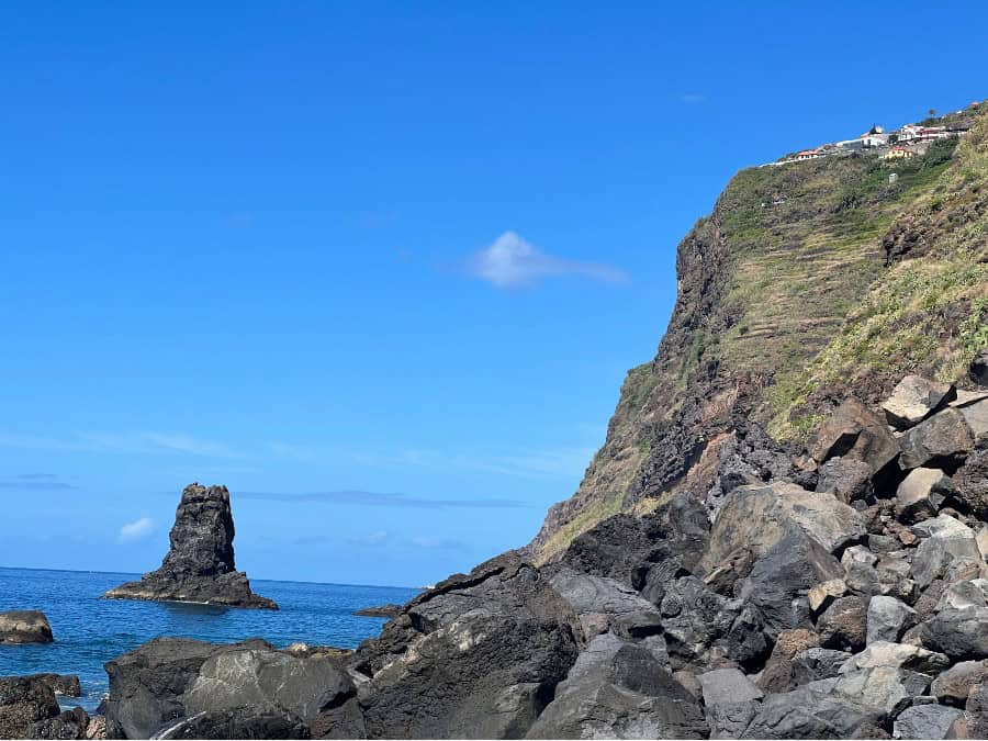 rock formation protruding from the ocean, with a settlement seen atop a huge cliff