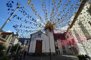 a white church with colourful garlands hanging from the street in Ponta Do Sol.