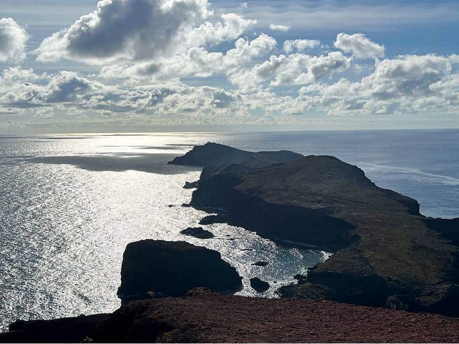 A dramatic silhouette of the São Lourenço peninsula jutting into the Atlantic, seen from the final viewpoint at Morro do Furado under a sky of thick clouds and shimmering sunlight on the sea.