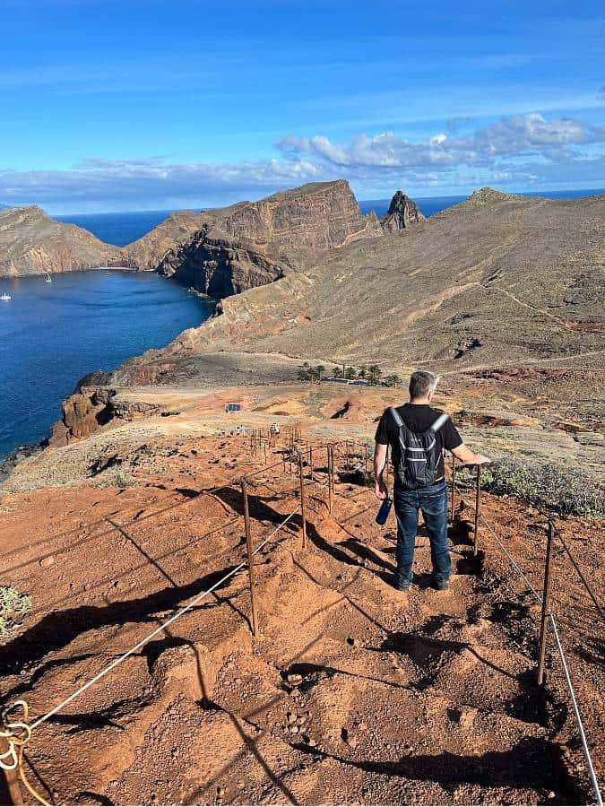 Richard descends a steep, dusty trail lined with rope railings, overlooking the rocky coastline and dramatic cliffs of Madeira’s Vereda da Ponta de São Lourenço.