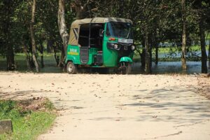 a green coloured tuk tuk parked near a lake