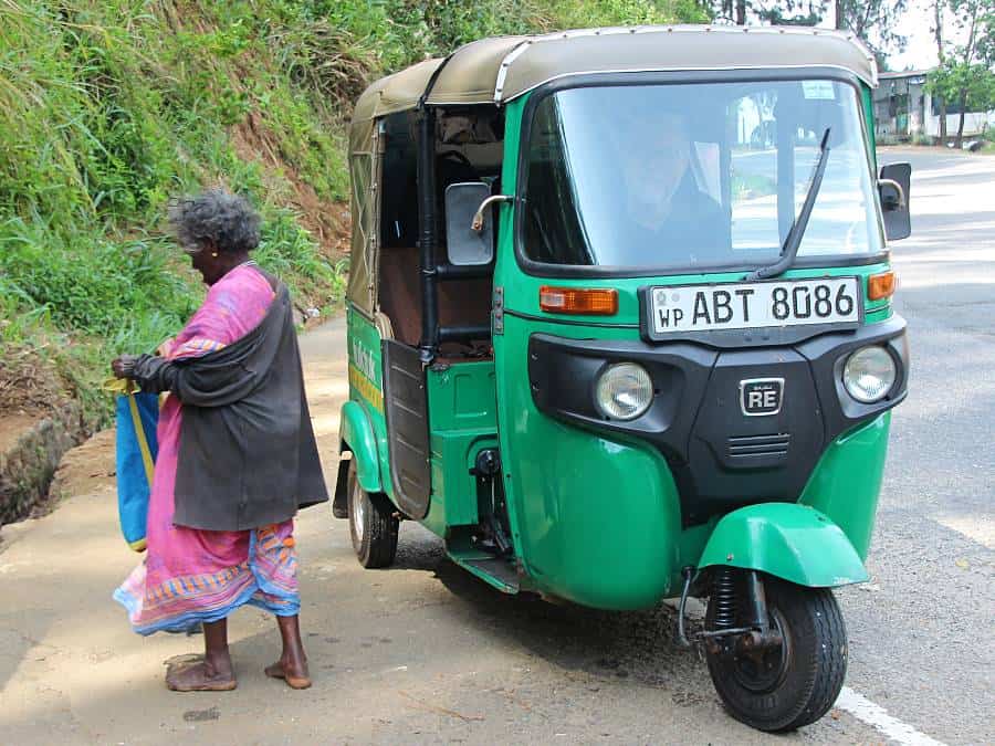 a lady dressed in pink walking away from a green tuktuk