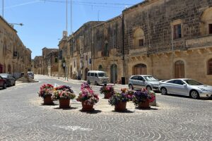 Quiet cobblestone street in Malta with flower-filled pots and historic stone buildings — a peaceful road trip stop perfect for slow mornings and scenic detours.