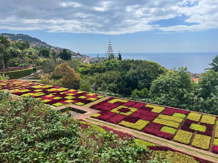 Patterned garden beds at Madeira Botanical Garden with coastal views and dramatic clouds.