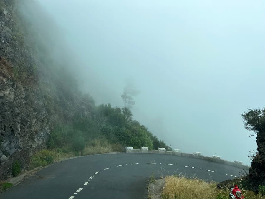 Fog rolling over a mountain road bend in Madeira, reducing visibility.
