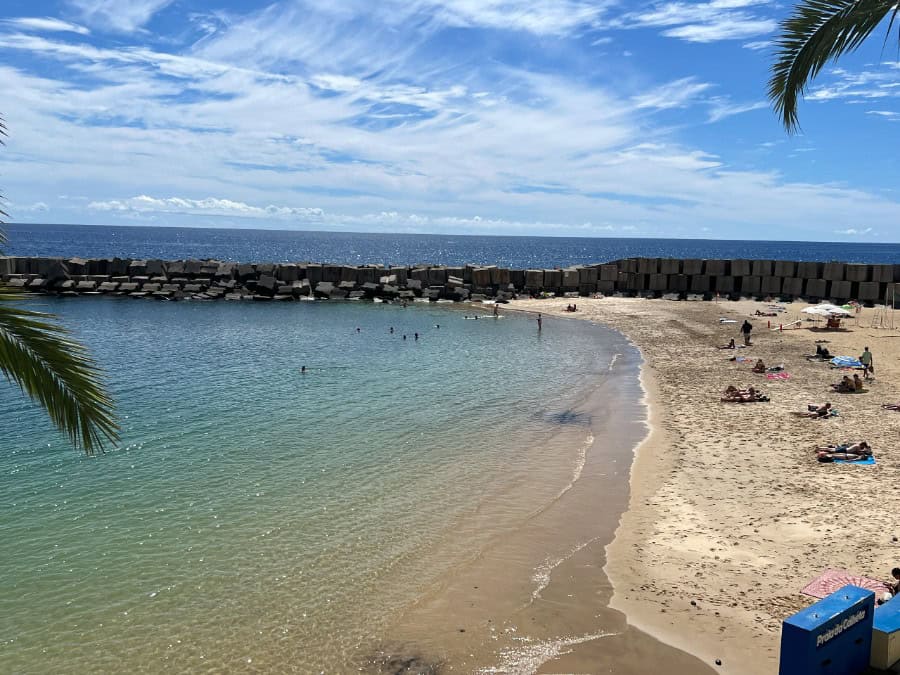 Sandy beach at Praia da Calheta with calm turquoise water and people sunbathing, Madeira.
