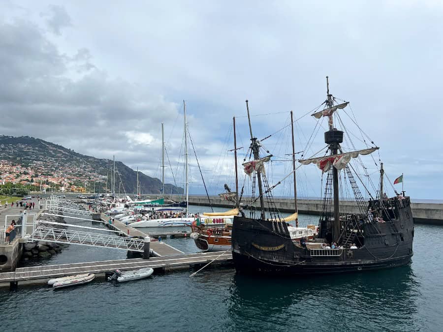 Replica sailing ship Santa Maria de Colombo moored at Funchal Marina with boats and hillside buildings, Madeira.