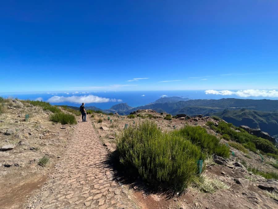Stone path near the Pico do Arieiro sign in Madeira, with mountains and ocean views ahead.