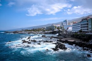 Puerto de la Cruz coastline in Tenerife with hotels, waves, black volcanic rocks and a seafront promenade.