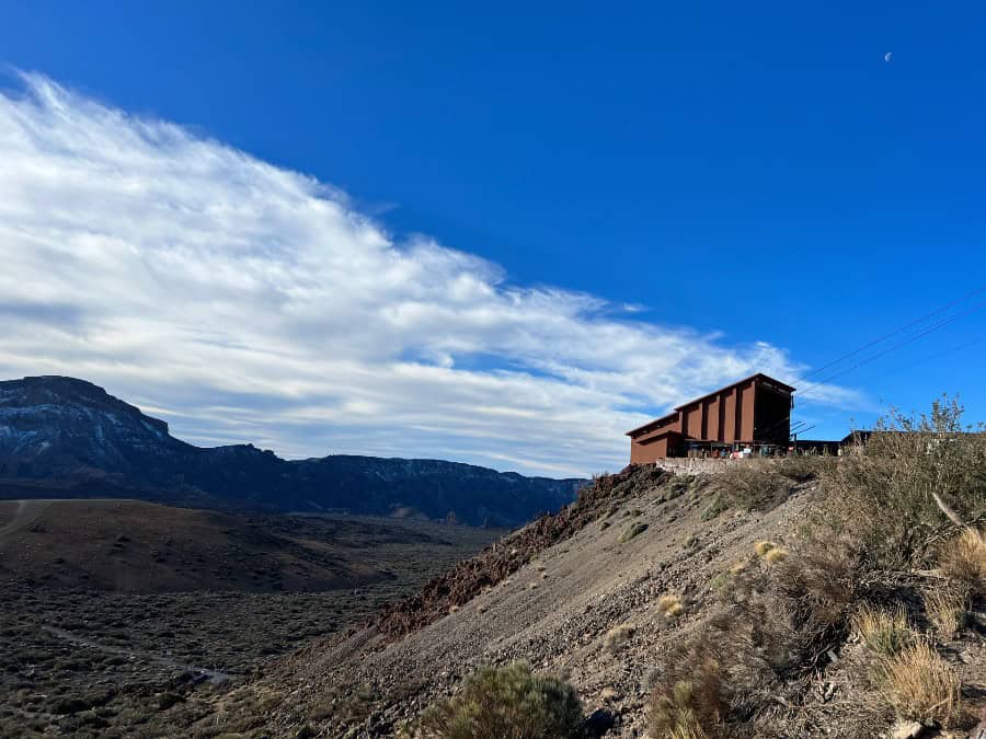 Teide National Park in Tenerife with volcanic landscape, mountains and a visitor centre under a blue sky.