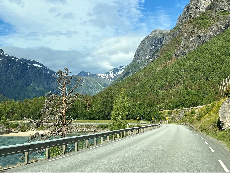 Scenic road through a green Norwegian valley with snow still on mountain peaks in June